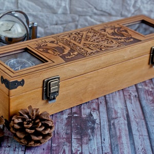 May include: A wooden box with a hinged lid and brass clasps. The box has three glass windows that show the interior. The box is decorated with an intricate design of a dragon and other mythical creatures. The box is sitting on a wooden surface.
