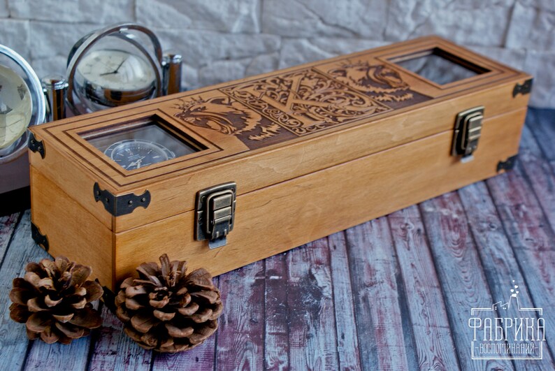 May include: A wooden box with a hinged lid and brass clasps. The box has three glass windows that show the interior. The box is decorated with an intricate design of a dragon and other mythical creatures. The box is sitting on a wooden surface.