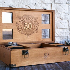 Puede incluir: Una caja de madera con tapa abatible y un interior de terciopelo. La tapa est&aacute; grabada con las palabras "Happy Birthday 50". La caja tiene un cierre y bisagras de lat&oacute;n.