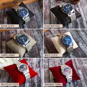 Puede incluir: Una colecci&oacute;n de cinco almohadas para relojes en diferentes colores y telas. Las almohadas est&aacute;n rellenas de un material suave y est&aacute;n dise&ntilde;adas para sujetar un reloj de forma segura. Las almohadas se muestran con un reloj en cada una. Las almohadas est&aacute;n disponibles en tela negra, material a cuadros, tela de arpillera, tela blanca, tela de terciopelo rojo y tela burdeos.