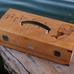 May include: A wooden fishing tackle box with a leather handle. The box has a ruler on the side and a fish and bucket design on the lid.