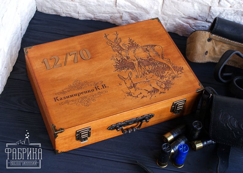 May include: A wooden box with a hinged lid, engraved with the number "12/70", the name "Kazimireko K.B.", and a design of deer in a forest. The box has a brass handle and metal clasps.