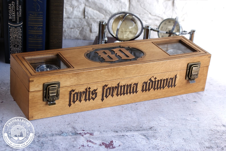Peut inclure: Une bo&icirc;te rectangulaire en bois avec deux fen&ecirc;tres en verre, des loquets en m&eacute;tal couleur laiton et le texte latin grav&eacute; "fortis fortuna adiuvat" sur le devant. Le couvercle pr&eacute;sente une plaque d&eacute;corative centrale avec les lettres "BD".