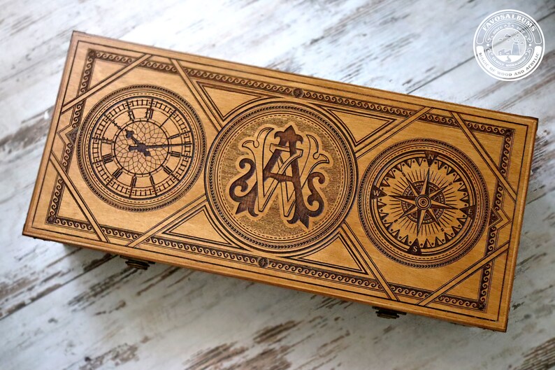 May include: A wooden box with a decorative design featuring a clock, compass, and monogrammed initials. The box is made of light wood and has a natural finish.