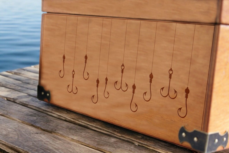 May include: A wooden box with a brown stain and metal corner accents. The lid of the box is decorated with an engraved design of multiple fishing hooks.