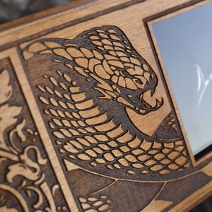 May include: A wooden box with a laser-engraved design of a snake on the front. The box has a small glass window on the right side. The box is labeled "Favosal Bums" with the text "Hall of Wood and Activity".