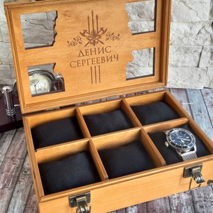 May include: A wooden watch box with a clear lid and six compartments lined with black fabric. The lid has an engraved design with the text "ДЕНИС СЕРГЕЕВИЧ".