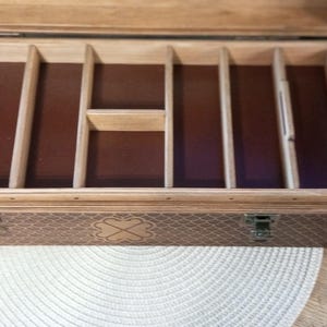 May include: Open wooden box with multiple compartments and a hinged lid. The interior features a dark brown lining and dividers. The exterior has a textured pattern and a metal clasp closure. The box is designed for storage.