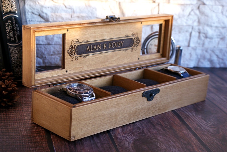 May include: A wooden watch box with a glass top and three compartments. The box is engraved with the name "ALAN R FOISY".