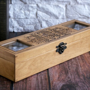 May include: A wooden box with a hinged lid and a metal latch. The box has two glass windows on the top, revealing the interior. The box is decorated with an intricate floral design.