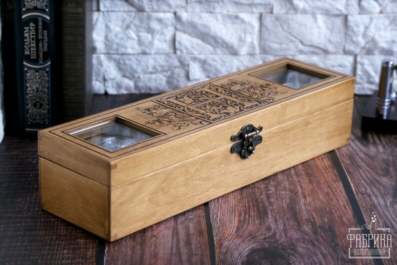 May include: A wooden box with a hinged lid and a metal latch. The box has two glass windows on the top, revealing the interior. The box is decorated with an intricate floral design.