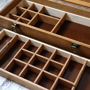 May include: A wooden box with two drawers, each with multiple compartments. The top drawer has a brown felt lining and the bottom drawer has a brown felt lining. The box has a brass latch and hinges.