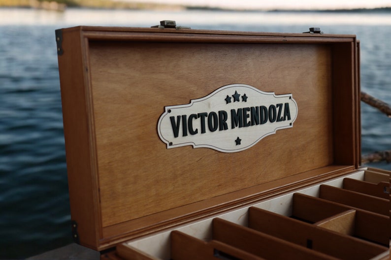 May include: A wooden box with a hinged lid and a sign that reads "VICTOR MENDOZA" with stars. The box has multiple compartments inside.