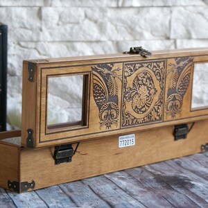 May include: A wooden box with a hinged lid, featuring an intricate design of owls and floral patterns. The box has two glass windows on the top and a brass latch. The box is made of light brown wood and has a label with the number 772015.