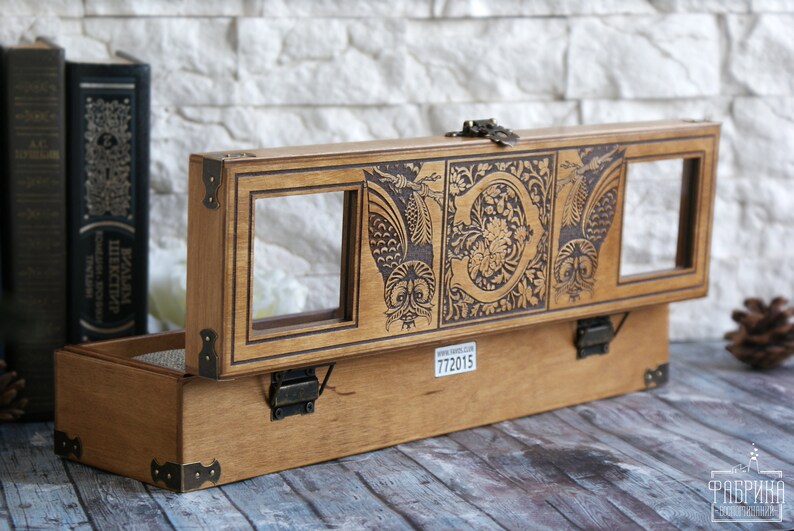 May include: A wooden box with a hinged lid, featuring an intricate design of owls and floral patterns. The box has two glass windows on the top and a brass latch. The box is made of light brown wood and has a label with the number 772015.
