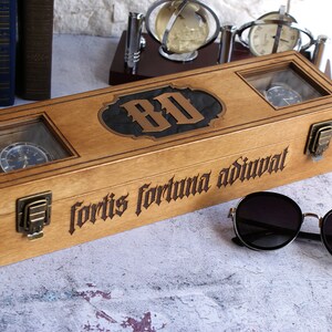 Peut inclure: Une bo&icirc;te &agrave; montres rectangulaire en bois avec deux fen&ecirc;tres en verre, des loquets en laiton et le texte grav&eacute; "fortis fortuna adiuvat" sur le devant. Le couvercle pr&eacute;sente une incrustation sombre centrale avec les lettres "BO".
