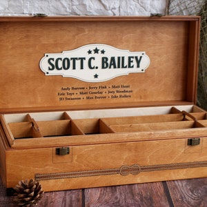 K&ouml;nnte beinhalten: Eine Holzkiste mit einem Scharnierdeckel und einem Seil-Design auf der Vorderseite. Der Deckel ist ge&ouml;ffnet und das Innere ist in F&auml;cher unterteilt. Die Kiste ist mit "SCOTT C. BAILEY" beschriftet und darunter befindet sich eine Namensliste.