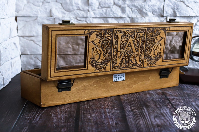 May include: A wooden box with a hinged lid, featuring a decorative design with the letters "LAN" and floral motifs. The box has two glass windows and a label with the text "www.zavod.co.uk 775710".