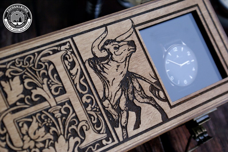 May include: A wooden box with a black and white engraved design of a bull and a decorative letter "F". The box has a glass window that displays a watch with black hands and a white face.
