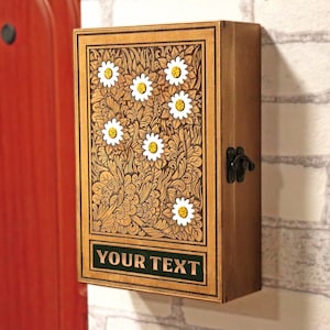 May include: A wooden box with a floral design carved into the front. The box has a hinged lid and a metal latch. The box is painted in a light brown color and has a green label with the text "YOUR TEXT" on it.