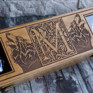 May include: Wooden watch box with two compartments for watches. The box is decorated with a carved wolf on each side and a monogrammed letter "M" in the centre.