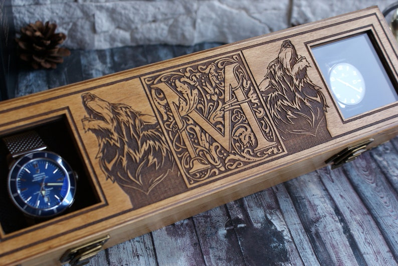 May include: Wooden watch box with two compartments for watches. The box is decorated with a carved wolf on each side and a monogrammed letter "M" in the centre.