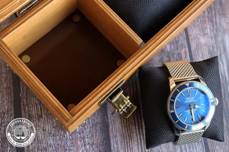 May include: A blue watch with a silver band and a blue face. The watch is sitting on a black cushion inside a wooden box.