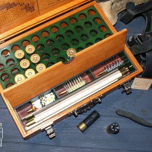 May include: A wooden box with a green felt lining and a compartment for shotgun shells. The box also has a drawer with cleaning supplies and a cleaning rod. The box is open and the drawer is pulled out. The box is labeled "Фабрика -воспроизведения-."