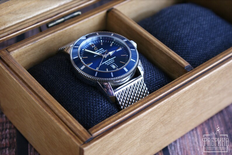 May include: A silver watch with a blue face and a mesh metal band is displayed in a wooden box with a blue velvet lining.