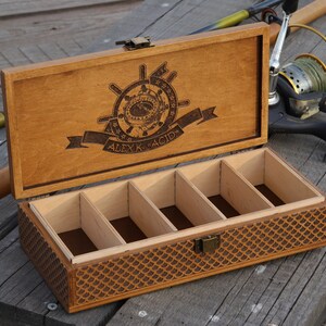 Op de afbeelding: Een houten doos met een scharnierend deksel en een decoratief gegraveerd ontwerp. Het deksel heeft een nautisch kompas en de naam "ALEX K. RACID". De doos heeft vijf compartimenten aan de binnenkant.