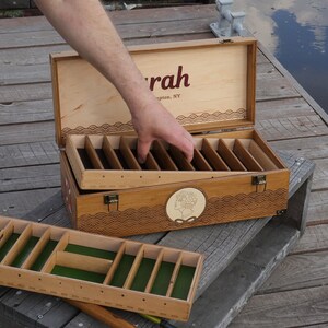 May include: A rectangular wooden storage box with a hinged lid featuring the text "rah" and "ington, NY". The box has a removable tray with green felt lining and multiple dividers. The exterior features a circular emblem and wave patterns.