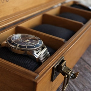 May include: A silver watch with a black face and a metal band is displayed in a wooden box with a brass latch. The box has a black velvet lining.