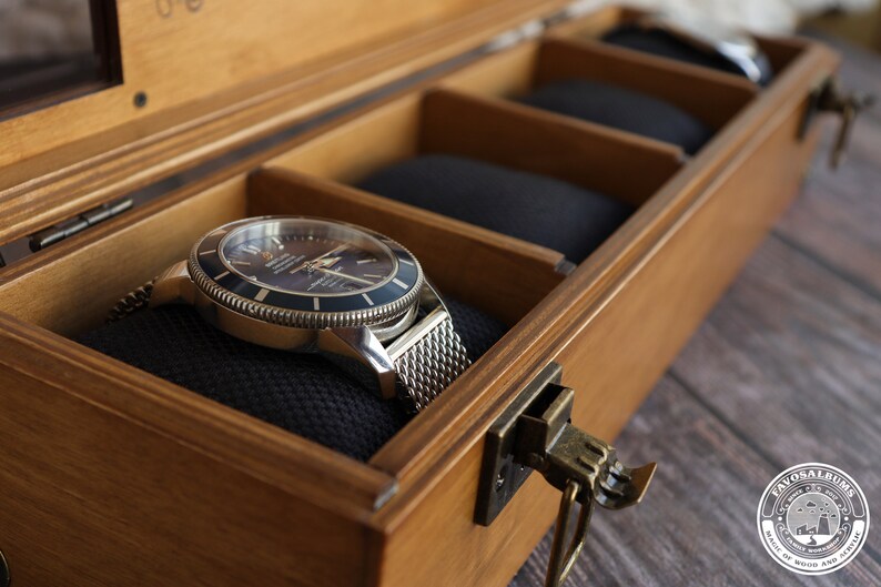 May include: A silver watch with a black face and a metal band is displayed in a wooden box with a brass latch. The box has a black velvet lining.