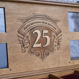 May include: A wooden box with a decorative engraved design that says "Happy Birthday, Dear Brother 25". The box has two glass windows on the top and a red velvet interior.