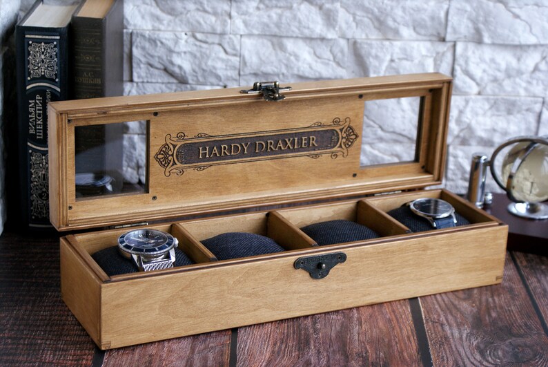 Pu&ograve; includere: Una scatola porta orologi in legno con un coperchio in vetro e quattro scomparti. La scatola &egrave; incisa con il nome "Hardy Draxler".