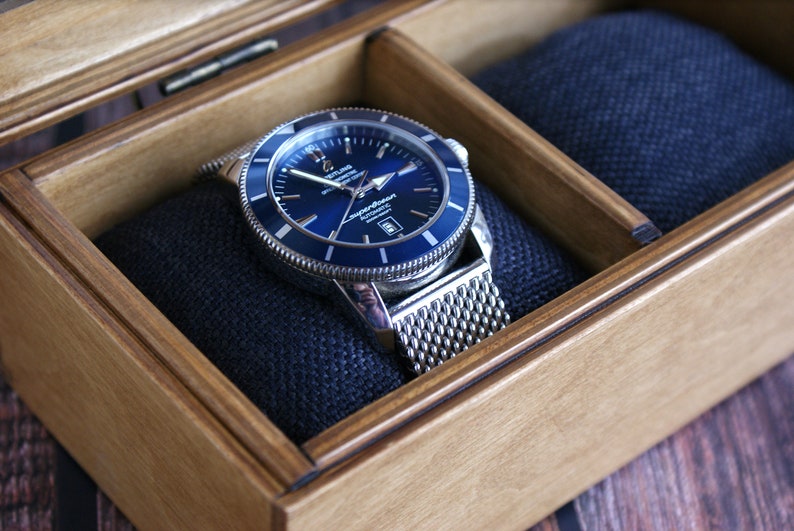 May include: A silver watch with a blue face and a mesh metal band is displayed in a wooden box with a blue velvet lining.