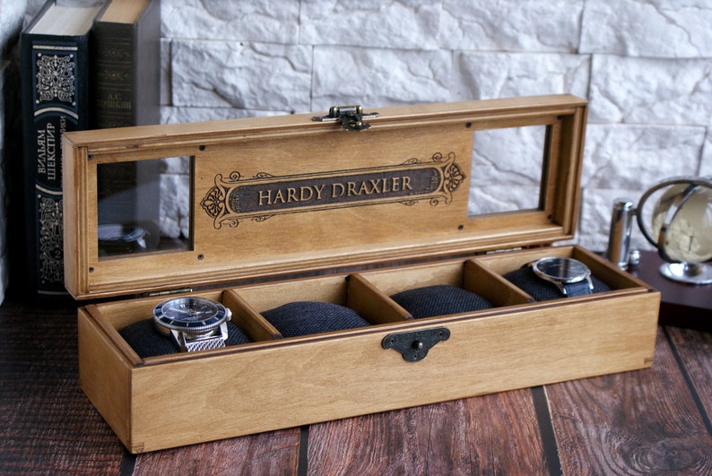 May include: A wooden watch box with a glass top and four compartments. The box is engraved with the name "Hardy Draxler".