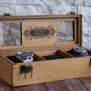 K&ouml;nnte beinhalten: Eine Holzuhrbox mit Glasdeckel und drei F&auml;chern. Die Box hat einen Messingverschluss und ist mit dem Namen "Lysenko Daniil" graviert.