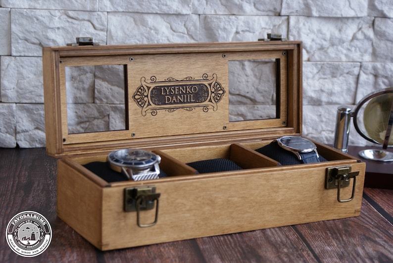 K&ouml;nnte beinhalten: Eine Holzuhrbox mit Glasdeckel und drei F&auml;chern. Die Box hat einen Messingverschluss und ist mit dem Namen "Lysenko Daniil" graviert.