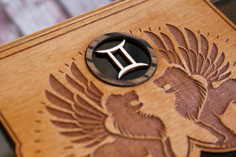 May include: A wooden box with a carved design of two winged lions. The box has a circular inlay with the Gemini zodiac symbol.
