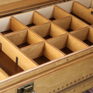 May include: A wooden box with a removable tray containing multiple compartments. The tray is made of light wood and has a natural finish. The box is made of a darker wood and has a more polished finish.