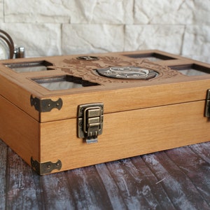 May include: A wooden box with a hinged lid and brass clasps. The lid features a carved design with a crest and initials. The box has a light wood finish and is made of natural wood.