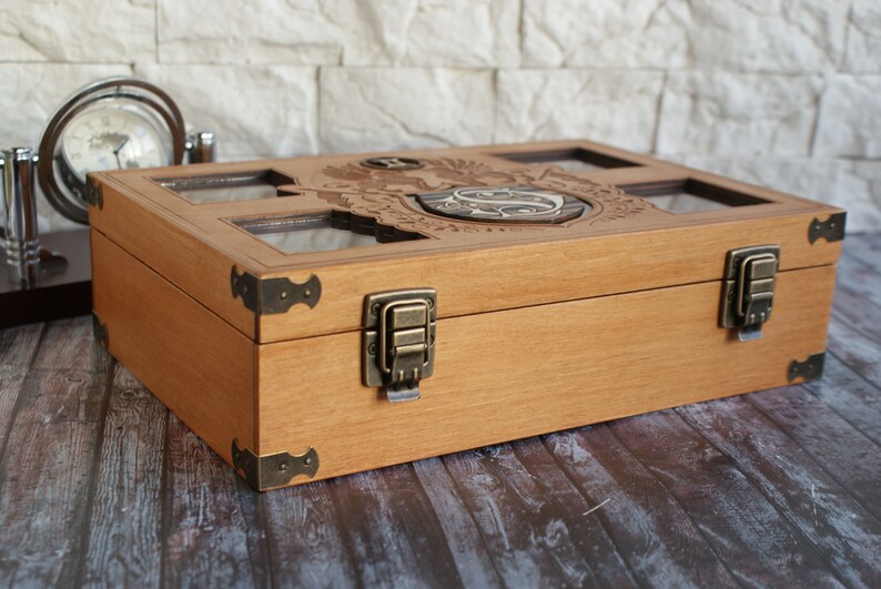 May include: A wooden box with a hinged lid and brass clasps. The lid features a carved design with a crest and initials. The box has a light wood finish and is made of natural wood.