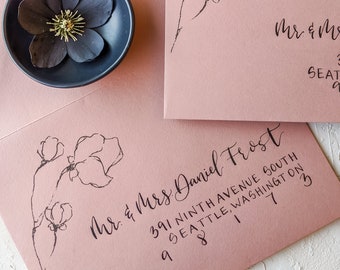 Pode incluir: Dois envelopes cor-de-rosa com caligrafia de tinta preta. O envelope superior tem o texto "Mr. & Mrs." e o envelope inferior tem o texto "Mr. & Mrs. Daniel Frost 391 Ninth Avenue South Seattle, Washington 98117". Ambos os envelopes têm um desenho floral.