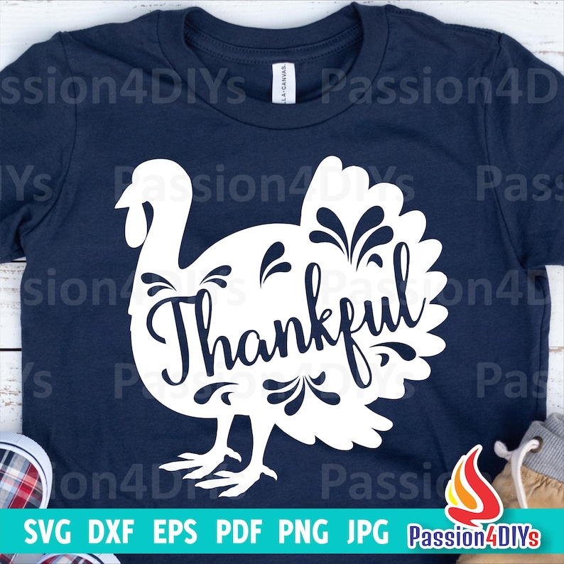May include: A navy blue t-shirt featuring a white silhouette of a turkey with the word "Thankful" inside the turkey's body. The turkey has a floral design on its feathers.
