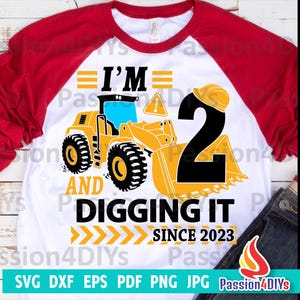 May include: A white and red baseball style t-shirt with a yellow construction vehicle and the text "I'm 2 and digging it since 2023".