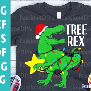 May include: A dark gray t-shirt with a green dinosaur wearing a Santa hat and holding a yellow star. The dinosaur is wrapped in colorful Christmas lights. The text "TREE REX" is printed on the shirt.