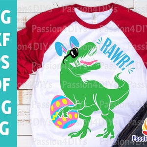 May include: A white t-shirt with a green dinosaur holding a colorful Easter egg. The dinosaur is wearing sunglasses and bunny ears. The text "RAWR!" is written in blue above the dinosaur.