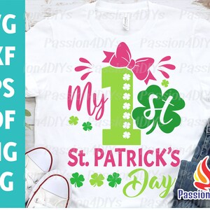May include: A white t-shirt with a green shamrock and the text "My 1st St. Patrick's Day" in pink. A pink bow is above the number one.