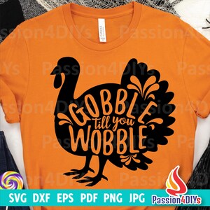 May include: A black and orange graphic design of a turkey with the text "Gobble till you wobble" inside the turkey silhouette. The design is on a bright orange t-shirt.